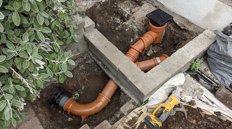New drainage pipework and gully installed beside a garden wall