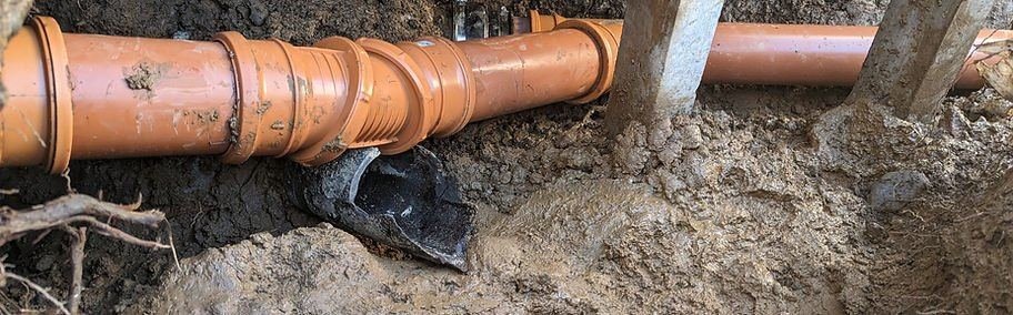 New orange plastic drain pipe and fittings laid in an open trench during a repair